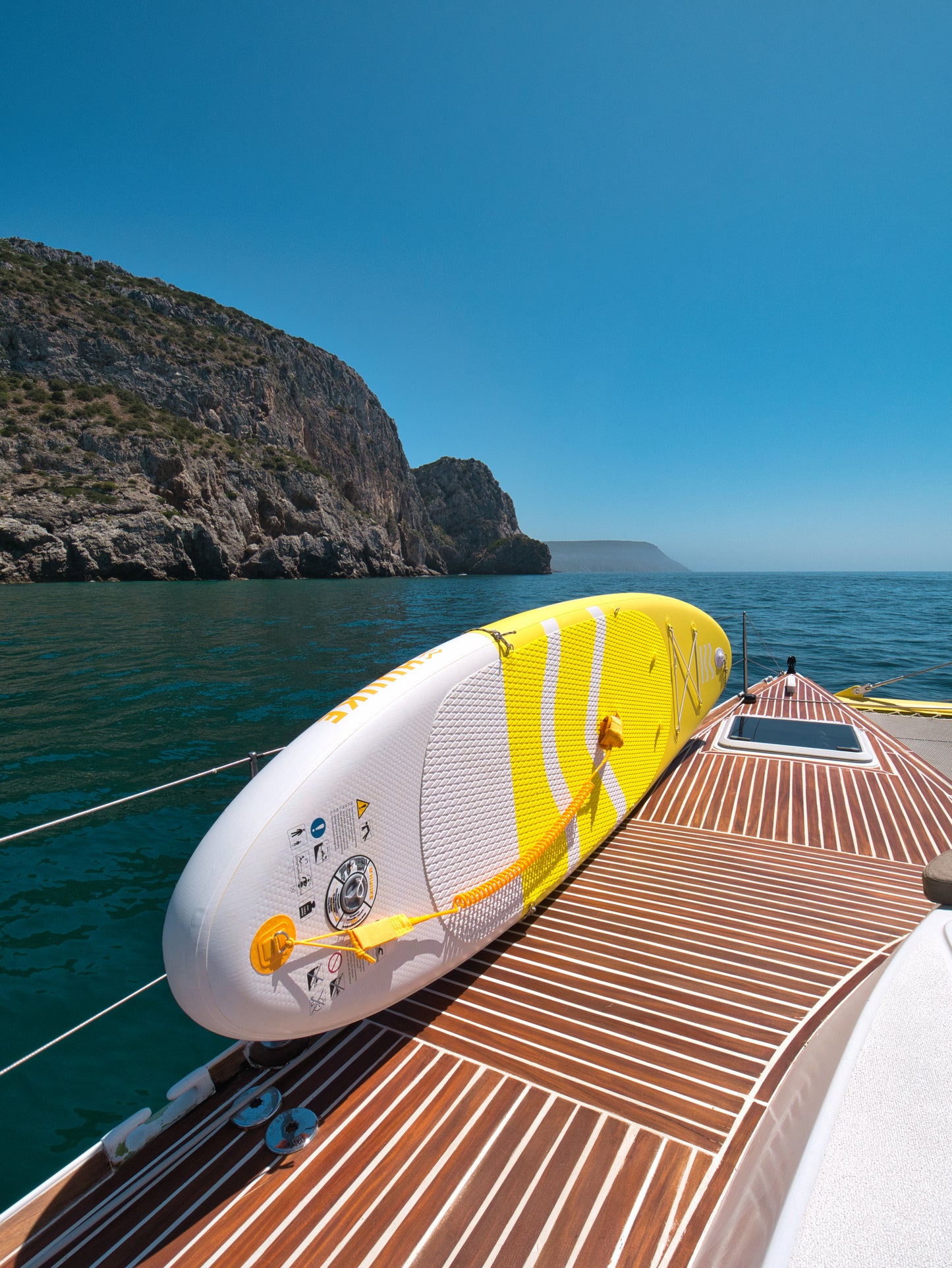 Paddleboard on sailboat deck with Serra da Arrábida limestone cliffs and Atlantic sea, Untold Blue water activities, Setúbal Peninsula