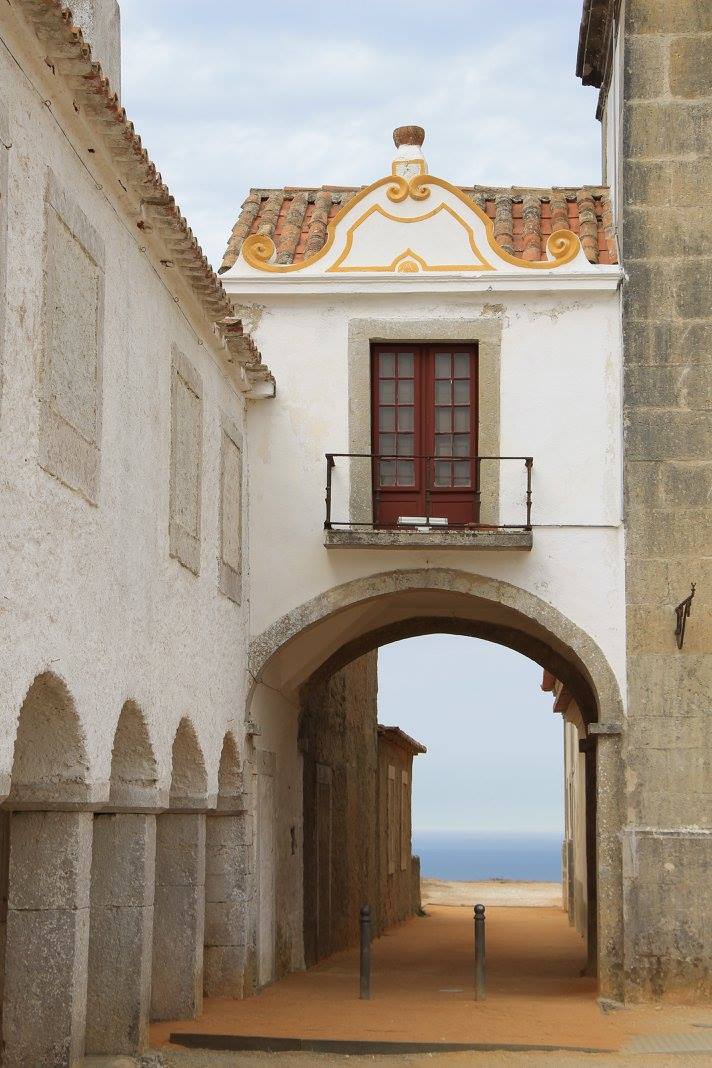 White Portuguese building with baroque pediment and stone street archway framing Atlantic ocean view, historic Sesimbra village, Setubal Peninsula, Segredos da Arrabida Portugal