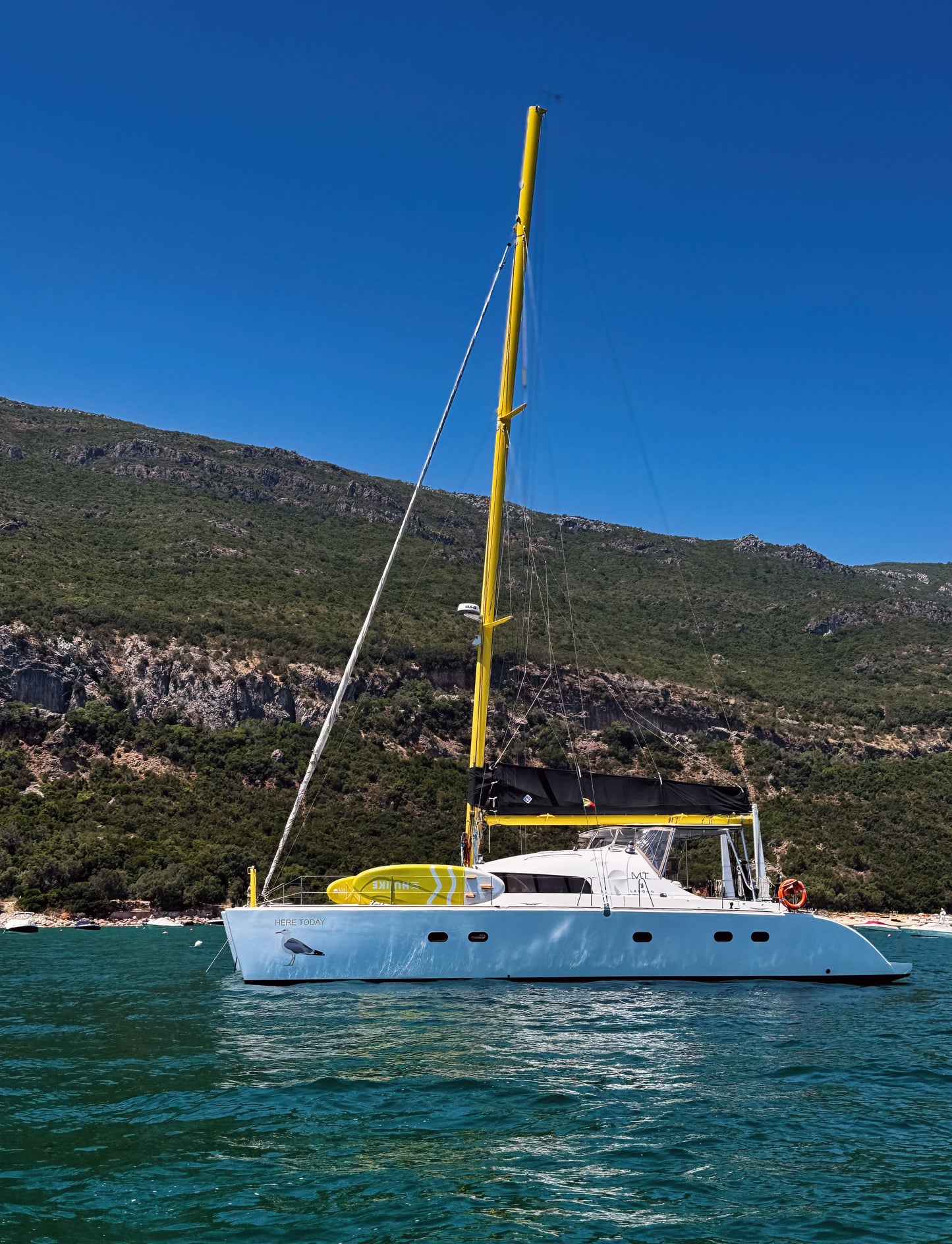 White catamaran anchored in sheltered Arrábida cove with Serra da Arrábida hills, private sailing experience