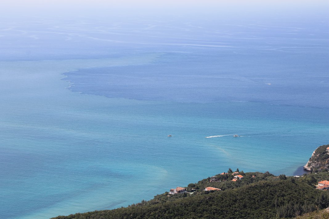 Aerial view of turquoise Atlantic sea and forested Arrábida coastline with village, Setúbal Peninsula
