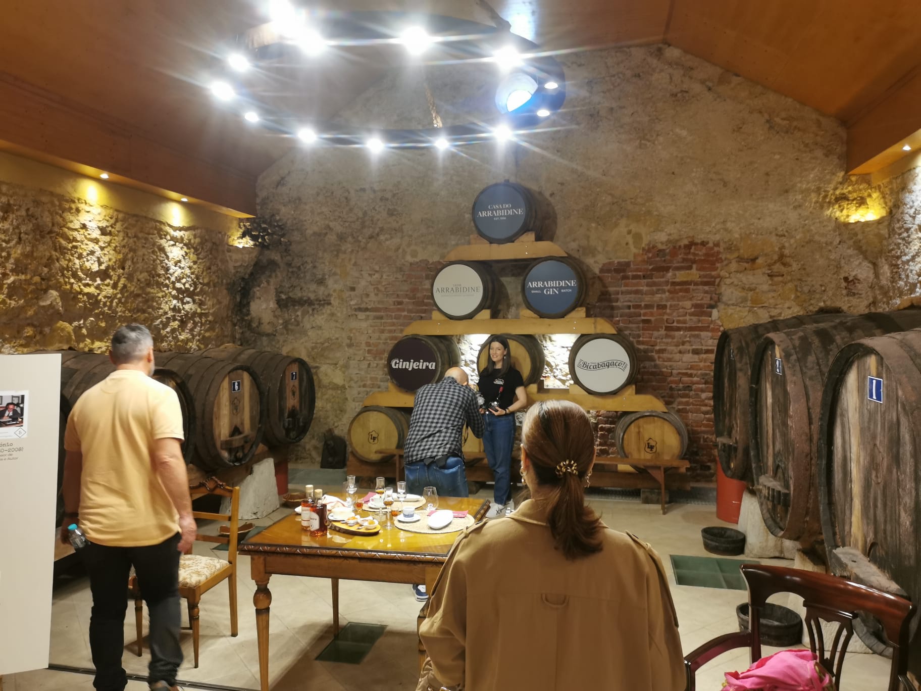 Guests inside Casa do Arrabidine wine cellar with oak barrels and string lights, Noite na Adega cellar evening experience, Setúbal Peninsula