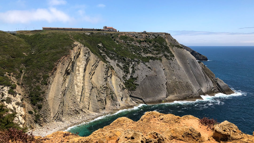 Dramatic limestone sea cliffs at Cabo Espichel with Atlantic ocean waves and historic sanctuary on clifftop, Setúbal Peninsula, The Untold Weekend