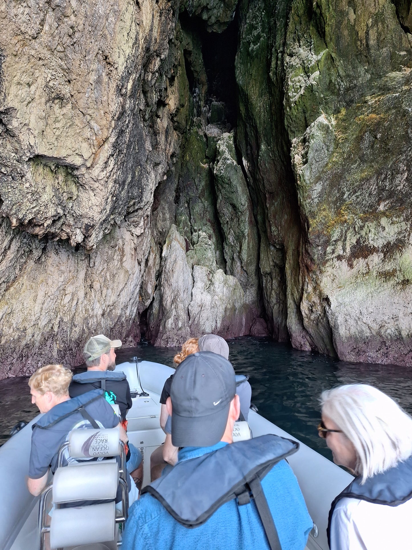 Guests on inflatable boat entering hidden sea cave, Arrábida coastline cave exploration, Setúbal Peninsula