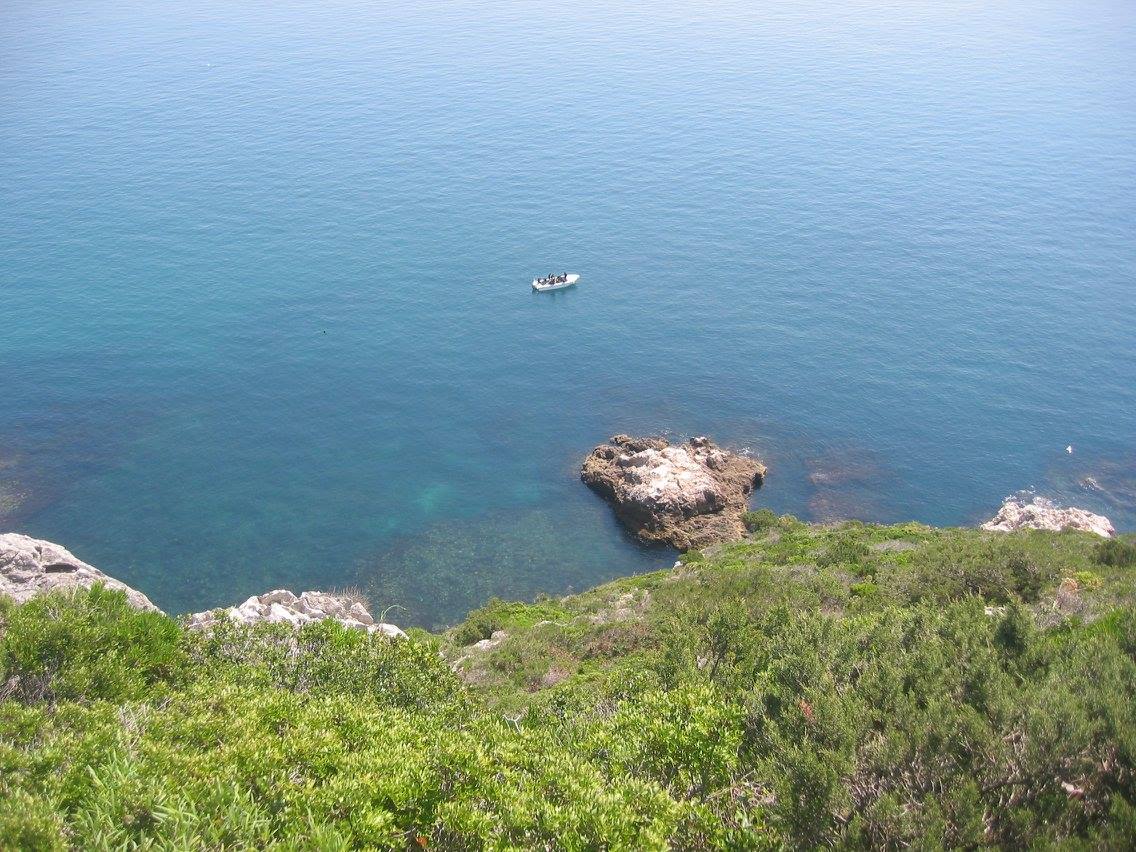 Turquoise Atlantic ocean coastline with rocky outcrops and small boat, elevated view, Costa da Arrabida, Arrabida Natural Park, Setubal Peninsula, The Untold Weekend