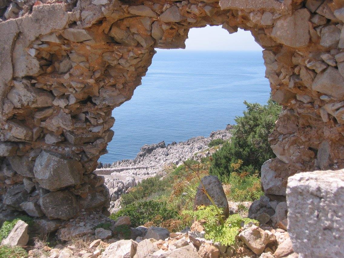 Stone archway of Forte da Baralha cliff ruins framing turquoise Atlantic ocean and rocky Arrabida coastline, Arrabida Natural Park, Setubal Peninsula, Portugal