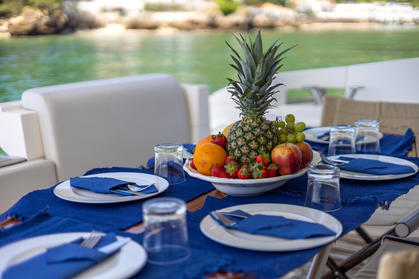 Elegant boat dining table with fresh fruit centerpiece and blue napkins, turquoise Arrabida cove backdrop, on-board dining experience, Setubal Peninsula, The Untold Weekend