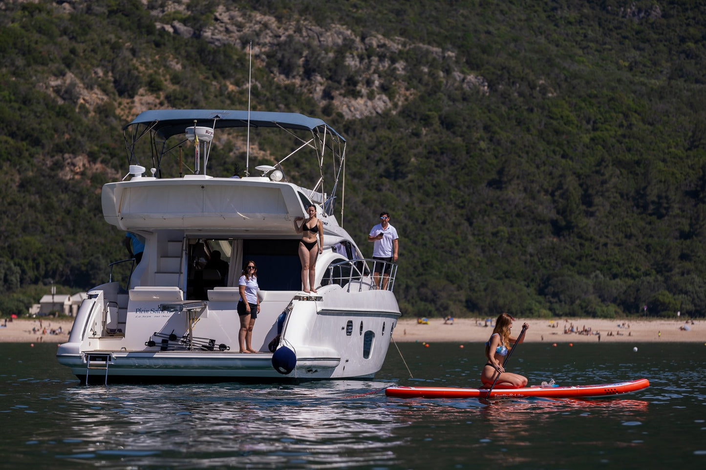 Luxury motor yacht anchored in Arrabida cove with woman on red paddleboard, Serra da Arrabida mountains backdrop, boat experience Setubal Peninsula, The Untold Weekend