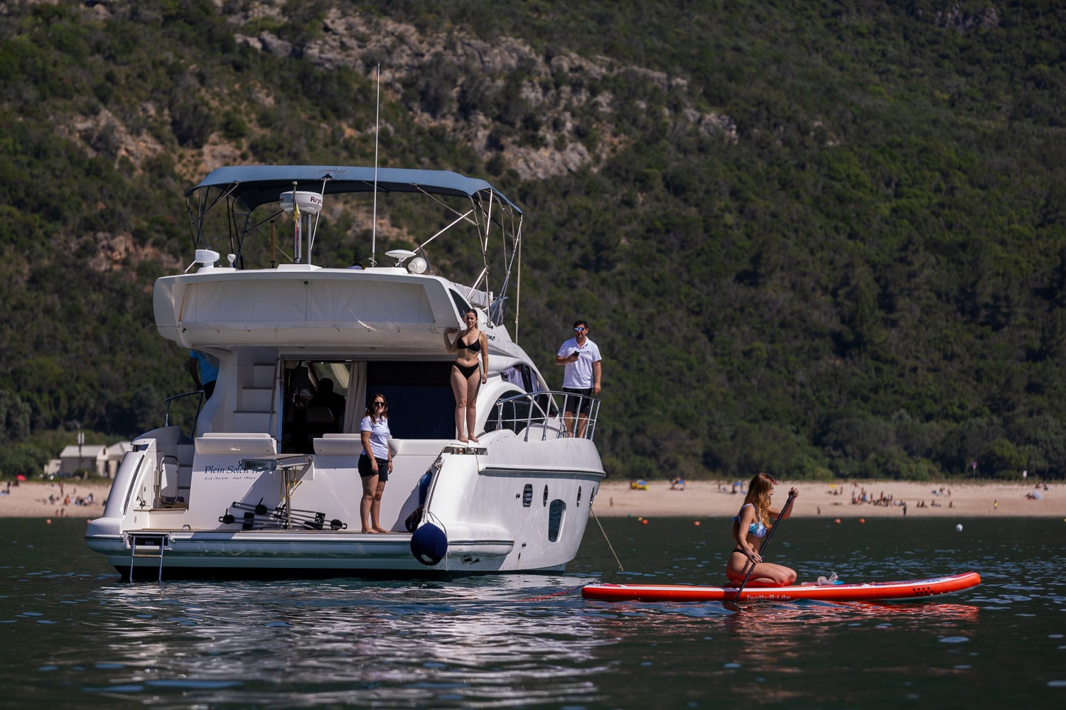 Luxury motor yacht anchored in Arrabida cove with woman on red paddleboard, Serra da Arrabida mountains backdrop, boat experience Setubal Peninsula, The Untold Weekend