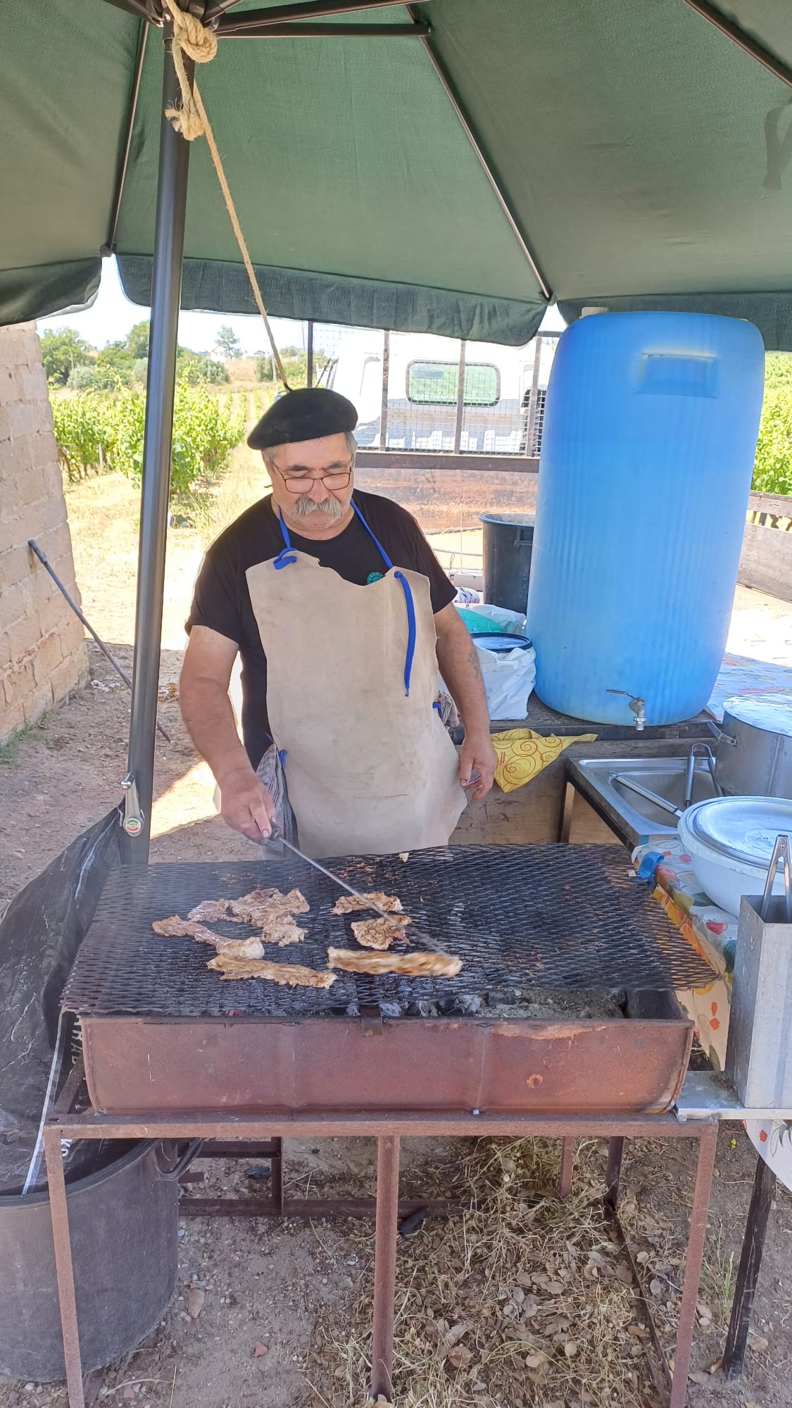 Local chef grilling fresh meat on traditional charcoal barbecue under canvas canopy, authentic rural dining experience, Serra da Arrabida region, Setubal Peninsula, Segredos da Arrabida