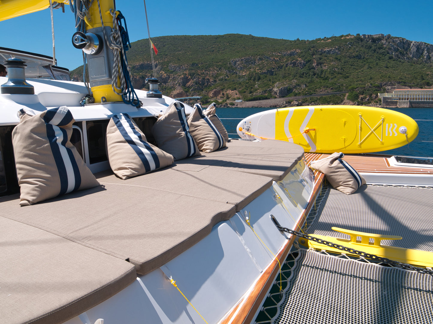 Luxury catamaran deck with cushions and yellow paddleboard, Serra da Arrabida mountains backdrop, boat experience Arrabida Natural Park, Setubal Peninsula, The Untold Weekend